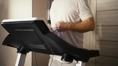 Man jogging on a treadmill at home. Middle-aged man in a grey t-shirt exerc.. Video stock 332162185