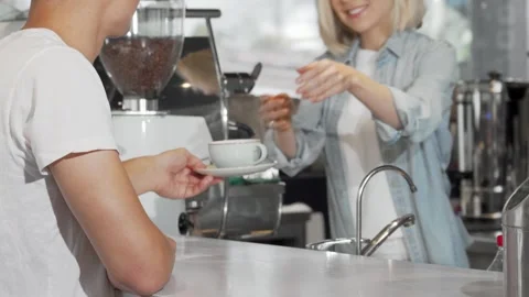 Man joyfully receiving a steaming cup of coffee from a friendly female barista Stock Footage 311944630