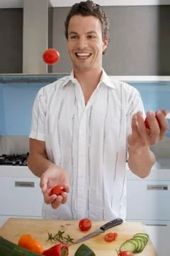 Man Juggling Tomatoes While Preparing Food In Kitchen Stock Photos