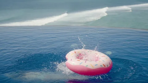 Man jump in inflatable ring with water splash in ocean view infinity pool Stock Footage 259159808
