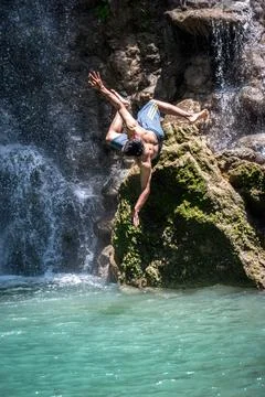 Man jumping into a clear blue pool under a waterfall. Stock-Fotos