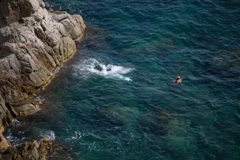 Man jumping from a cliff into the deep blue sea Stock Photos