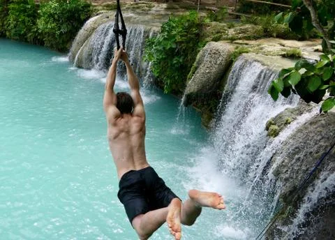 Man jumping from cliff into natural pool with waterfall, Siquijor, Philippines Stock Photos