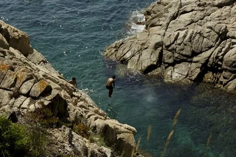 Man jumping off the cliff into the ocean. Fun summer lifestyle. Stock Photos
