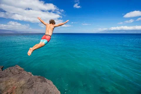Man jumping off cliff into the ocean Stock Photos