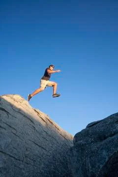 A Man Jumping Off A Large Boulder Stock Photos