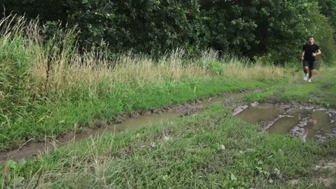 Man jumping over puddle while running on muddy forest trail Stock Footage 346533602