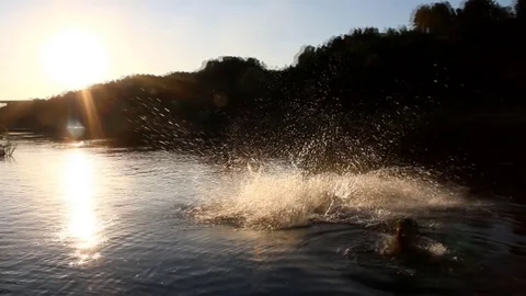 A man jumps in the river at sunset Stock Footage 84295818