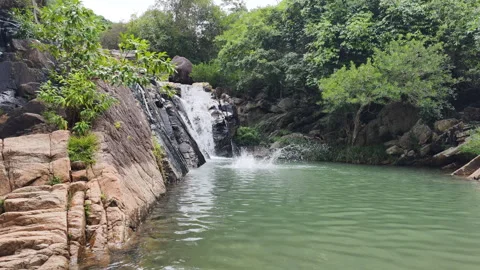 A man jumps from rocks into a refreshing waterfall pool. Hidden waterfall Stock Footage 323187963
