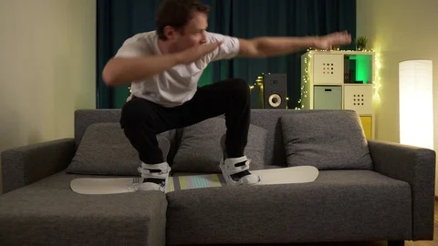 A man jumps on a snowboard on the couch Stock Footage 129387540