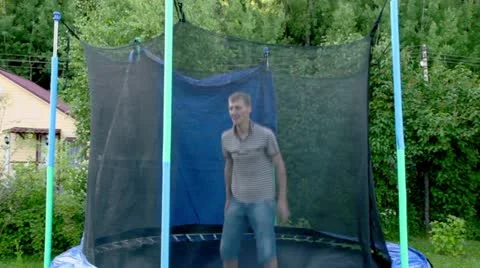 Man jumps on trampoline at background of country house Stock Footage