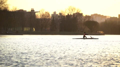 Man is kayaking alone in river at sunset on city background in slow motion Видео 131652355
