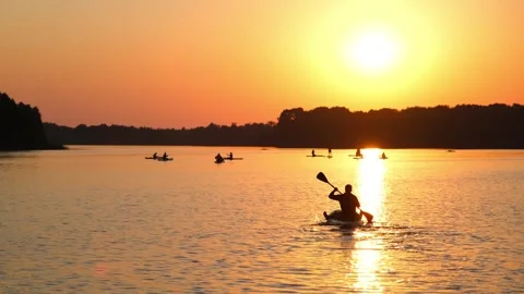 A man kayaking on a lake at sunset. Silhouetted paddler moves across reflective Stock Footage 340356908