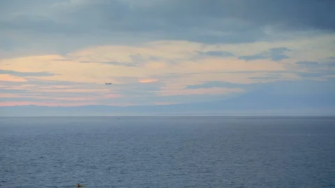 A man is kayaking in ocean in sunset while airplane is landing Stock Footage 113553456