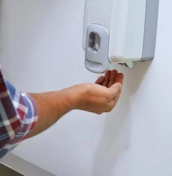 A man is kept hands under an automatic wall mounted sanitizer dispenser. Foto stock