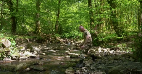 A man in a khaki uniform runs in the forest across the stream and washes himself Stock Footage 155259343
