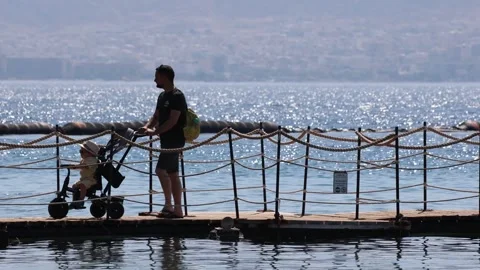 Man with a kid in a stroller walking along the pier in Dolphin Reef Stock Footage 280176843
