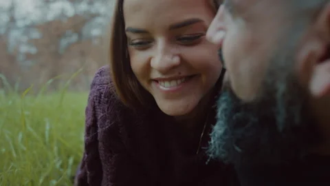Man kisses his partner while lying down on grass near to trees Stock Footage 275277434