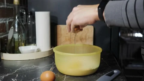 A man in the kitchen adds eggs to a bowl. Stock Footage 143948375