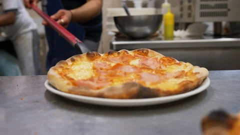 A man in the kitchen with a big spatula puts pizza on a plate. Stock Footage 104667914