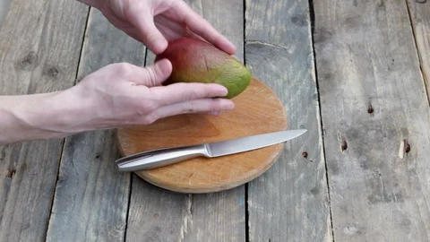 A man in the kitchen cut a wrinkled mango. Mango fruit cut into pieces. Stock Footage 129625781