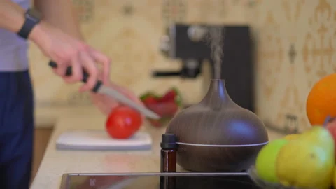 A man in a kitchen cuts vegetable. An aroma diffusor is standing on a table in Video stock 210069595
