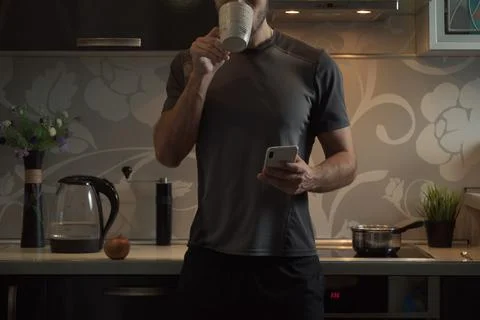 The man in the kitchen drinks from a mug. Mobile phone in his hand Foto stock