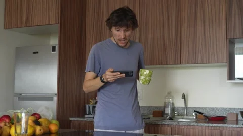 A man in a kitchen engrossed in his phone suddenly becomes very angry, screaming Stock-Footage 321359605