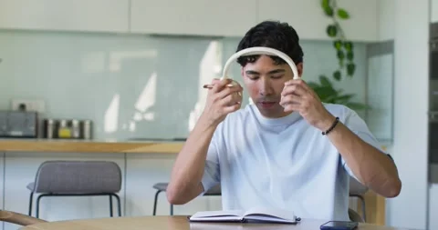 Man in kitchen glancing notes, reaching for headphones, checking earcups, Stock Footage 340011778
