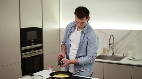 Man on a kitchen. Handsome tall guy cooking breakfast, making omelette adding Stock Footage 123939124