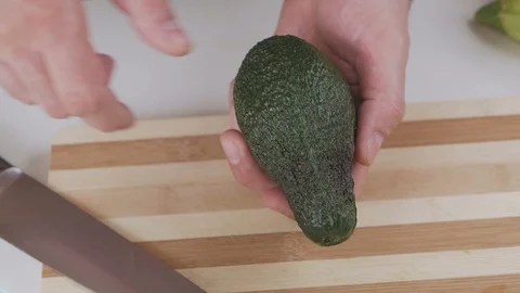 A man with a kitchen knife extracts a bone from a ripe avocado. Video stock 101807865