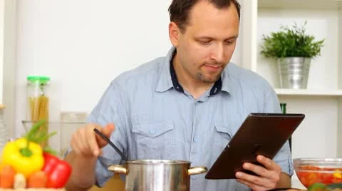 Man in kitchen looking at recipe on electronic tab during cooking Stock Footage 8983578