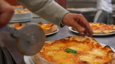Man in the kitchen, on a metal table, with a pizza cutter cuts it into 4 pieces. Stock Footage 104672122