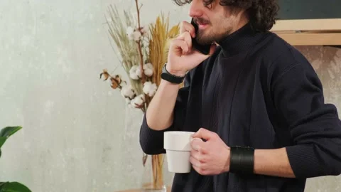 Man on kitchen is smiling, drinking coffee and talking on a smart phone. Stock Footage 154204639