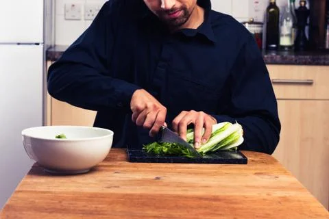 Man at kitchen table chopping lettuce Photos