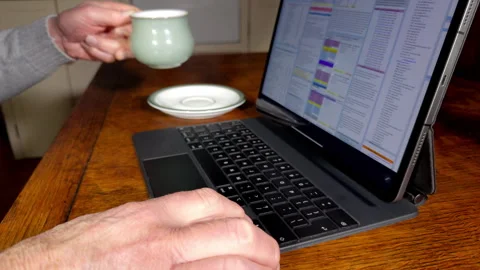 A man at a kitchen table with a hot drink, using a tablet computer and keyboard. Stock Footage 296221793