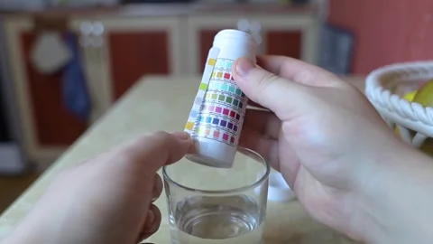 A man in the kitchen tests tap water quality with a test strip. Home testing for Stock Footage 327855818