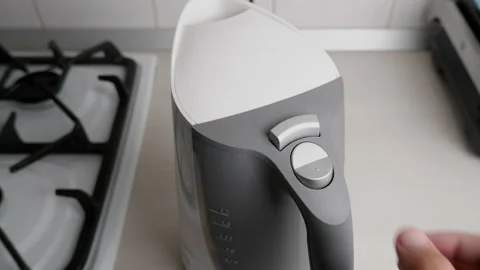 The man in the kitchen turns on a white electric kettle with a gray handle. Stock Footage 155249770