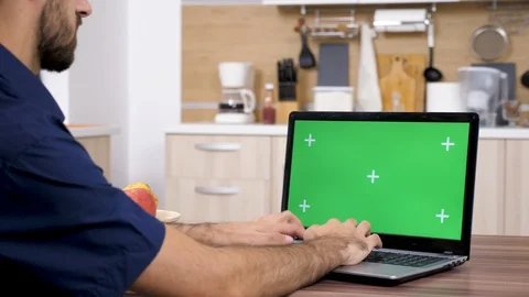 Man in the kitchen typing on laptop keyboard with green screen Stock Footage 97267145