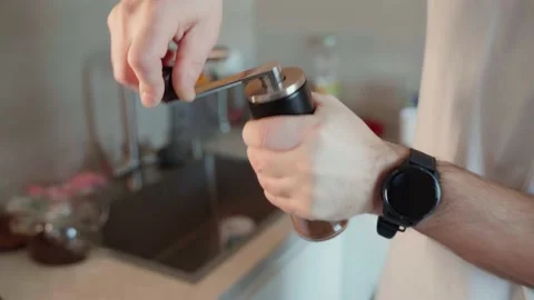 A man in the kitchen uses a tool to grind coffee beans. He grinds coffee into Stock Footage 233284788