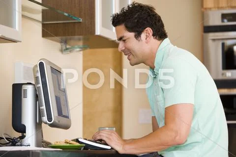 Man in kitchen using computer and smiling Stock Photos