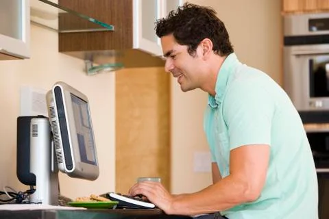 Man in kitchen using computer and smiling Stock Photos