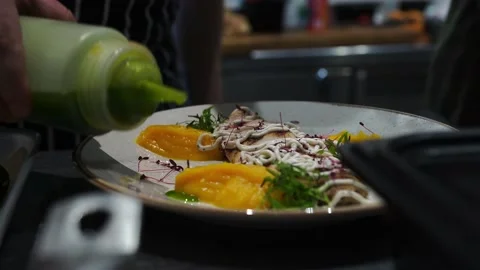 Man in kitchen waters, decorates a dish before serving with green sunflower oil Stock Footage 141100941