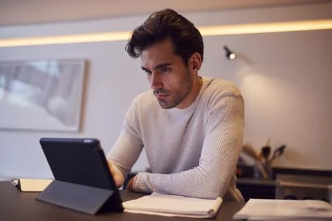 Man In Kitchen Working Or Studying From Home Using Digital Tablet Stock Photos