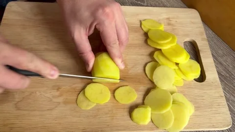 Man on kithcen uses knife to cut fresh raw potatoes on wooden cutting board Video stock 269246516