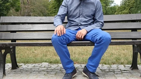 A Man with Knee Joint Pain sitting on a Bench in Park Stock Footage