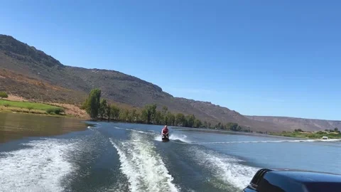 Man kneeboarding in choppy wake behind speed boat on Bulshoek Dam, South Afri Stock Footage 181487804