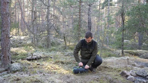 Man kneeling with backpack in peaceful pine forest wilderness Stock Footage 333690435