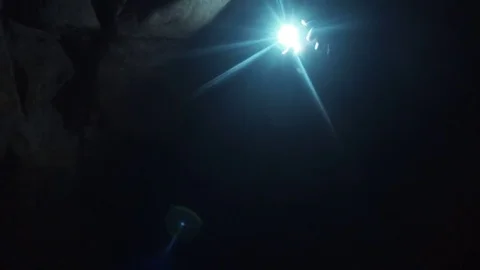 Man kneeling on ground in narrow cave explores the walls with help flashlight Video stock 80053599
