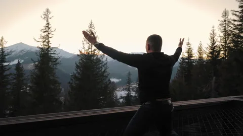 Man kneeling with raised hands in prayer before majestic mountains at sunset Stock Footage 304044758